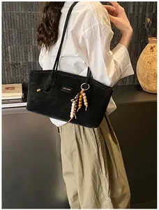 Detail of a large black suede tote bag with wooden bead charm on a shoulder strap