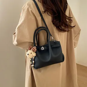 Minimalist black lychee texture bucket bag with plush bear charm worn by a model