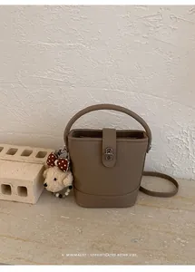 Detailed view of brown litchi leather bucket bag with metal buckle and plush charm