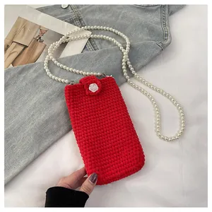 Close-up of red knitted lion dance phone bag featuring pearl strap and white rose