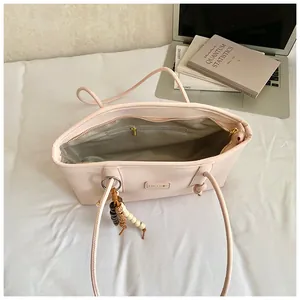 Detail of light pink tote bag interior featuring zipper pocket and chic beaded charm