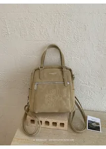 Detail der khakifarbenen Wildleder-Tasche mit Logo-Prägung und silbernem Reißverschluss