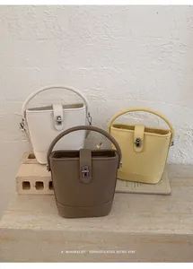 Three minimalist bucket bags in cream, yellow, and brown with lychee grain leather texture