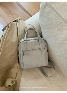 Detail der hellgrauen Ledertasche mit geprägtem Schriftzug auf einem Sofa