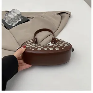 Detail of dark brown leather hobo bag featuring silver rivets and curved handle design
