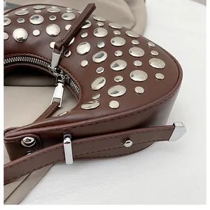Close-up of silver studs on a dark brown leather crescent bag with metal zipper detail