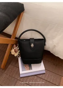 Close-up of black lychee grain bucket bag with silver metal lock and teddy bear charm