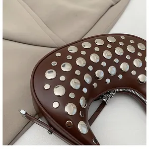 Detail of dark brown leather crescent bag with silver metal rivets and zipper