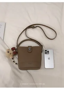 Detail of tan leather bucket bag featuring a rotating metal clasp and bear charm