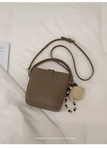 Detail shot of a brown bucket bag with lychee texture and a cute plush bear charm