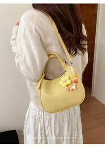 Détail du sac hobo en cuir jaune avec breloques fleurs tricotées porté par un modèle