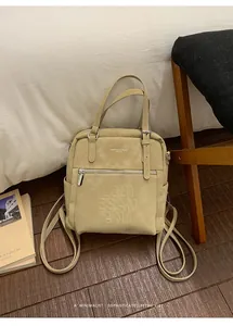 Detail eines beigefarbenen Lederrucksacks mit geprägten Buchstaben und Silberbeschlägen