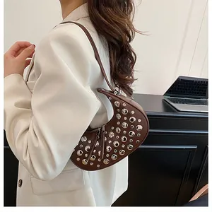 Detail of a dark brown crescent bag with silver rivets worn over a cream blazer