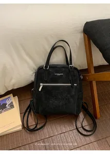 Detail eines schwarzen Wildleder-Rucksacks mit Buchstabenprägung auf Holzfußboden