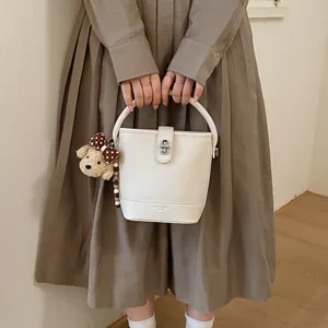 Chic cream bucket bag with litchi leather texture and a cute plush bear pendant