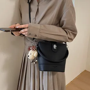 Chic black litchi grain bucket bag with metallic twist lock and cute plush puppy charm