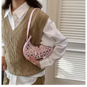 Pink crescent underarm bag with silver stud accents worn over a stylish knit vest