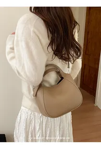 Détail du sac seau en cuir grainé taupe avec un design unique en arc semi-circulaire