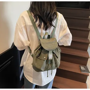 Outdoor view of an olive green checkered nylon backpack on wooden stairs with buckle detail