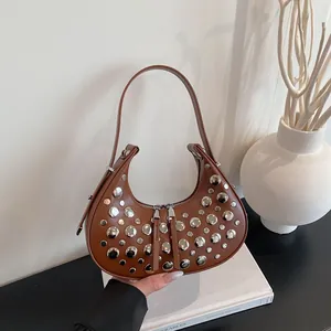 Brown leather crescent bag with silver rivets on a minimalist white book background