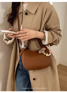 Détail du sac seau en cuir marron avec breloque florale perlée et logo de la marque