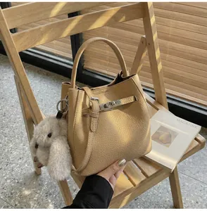 Dettaglio della borsa a secchiello in pelle beige con chiusura rotante e charm di peluche