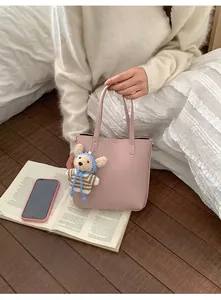 Détail du sac seau en cuir litchi rose avec charm ours en peluche sur literie blanche