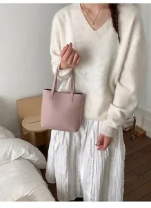 Détail d'un sac seau rose à grain litchi porté par un mannequin en tenue blanche