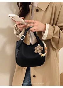Détail du sac seau en cuir noir avec breloque fleurie en perles sur un trench-coat kaki