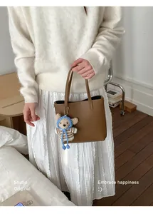 Gros plan du sac seau en cuir marron avec charm ours et texture grainée élégante