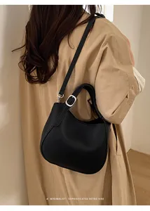 Détail du sac seau en cuir grainé noir avec finitions argentées sur un trench-coat kaki