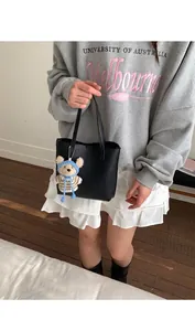Détail d'un sac cabas en cuir grainé noir avec un pendentif mignon en forme d'ours au crochet