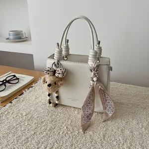 Elegante borsa a mano quadrata crema con manici a nodo e ciondolo a forma di orso