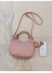 Sac seau rose en cuir grainé avec pendentif perle et nœud, comparé à un téléphone