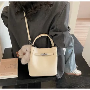 Dettaglio della borsa a secchiello in pelle crema con chiusura in metallo e ciondolo peluche