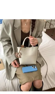 Détail du sac seau en cuir beige avec pendentif cheval en bois et smartphone pour l'échelle