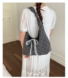 Detailed side view of grey canvas tote bag with black polka dots and white lace bow