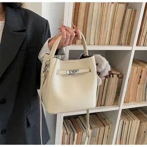 Dettaglio della borsa a secchiello in pelle crema con chiusura a scatto su una modella