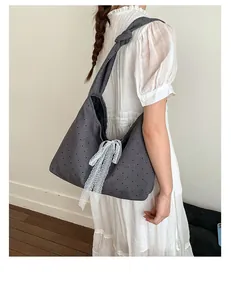 Detail of grey polka dot canvas hobo bag with a white lace bow shown on a shoulder