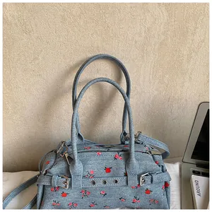 Detail of light blue denim lunch bag with red floral print and adjustable shoulder strap