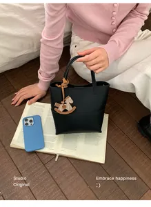 Détail du sac seau en cuir noir avec un pendentif cheval à bascule en bois sur la poignée