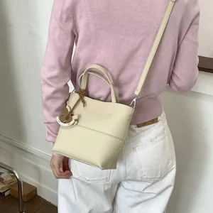 Sac seau chic en cuir blanc crème avec breloque cheval porté par un mannequin stylé