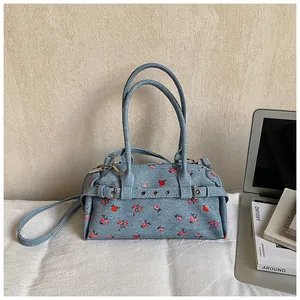 Detail of light blue denim pillow bag with red rose print and silver metal buckles
