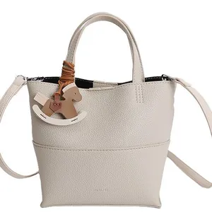 Sac seau minimaliste en cuir beige avec poignée supérieure et breloque cheval à bascule