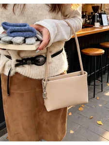 Detail view of a beige minimalist bucket bag with silver chain on model in street setting