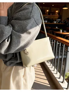 Detail of minimalist cream leather shoulder bag with crescent metal hardware accent