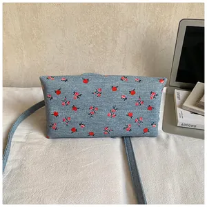 Detail of blue denim floral crossbody bag showing red flower pattern on a white desk