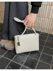 Close-up of minimalist cream white PU leather bucket bag with silver metal charm detail