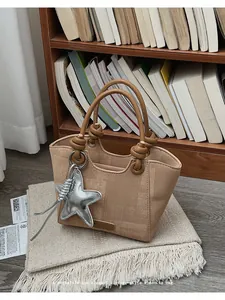 Close-up of woven bucket bag with leather handle and star charm on a beige blanket