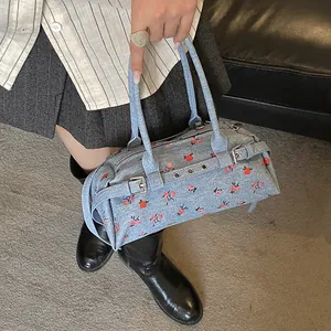 Detail of blue denim shoulder bag with red floral print and silver metal buckles